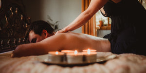 Man gets massage on bed with candles on tray next to him.