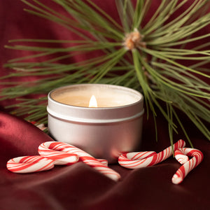 A lit Skinny Dip Candle sits on red satin, surrounded by miniature candy canes and a bundle of pine needles behind it.