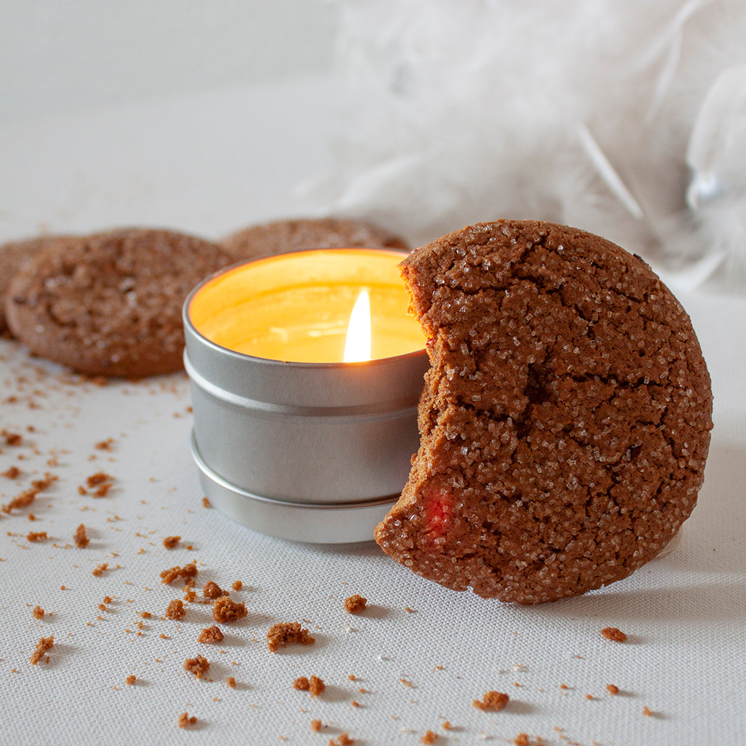 A fresh gingersnap cookie with a bite out of it sits against a lit Skinny Dip Candle. Crumbs litter the table.